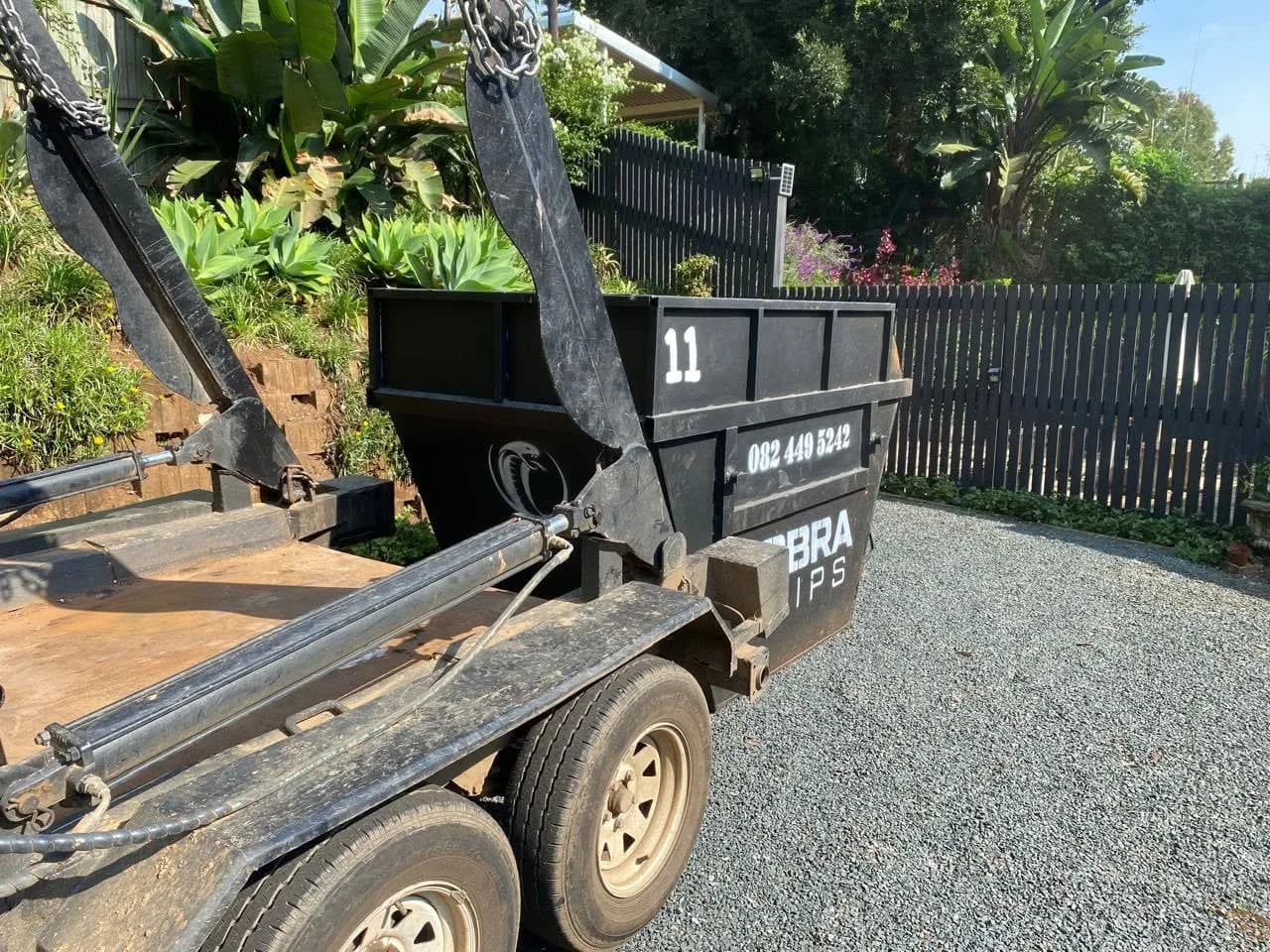 Kobra Skip number 11 being positioned by the crane arm on a gravel driveway.