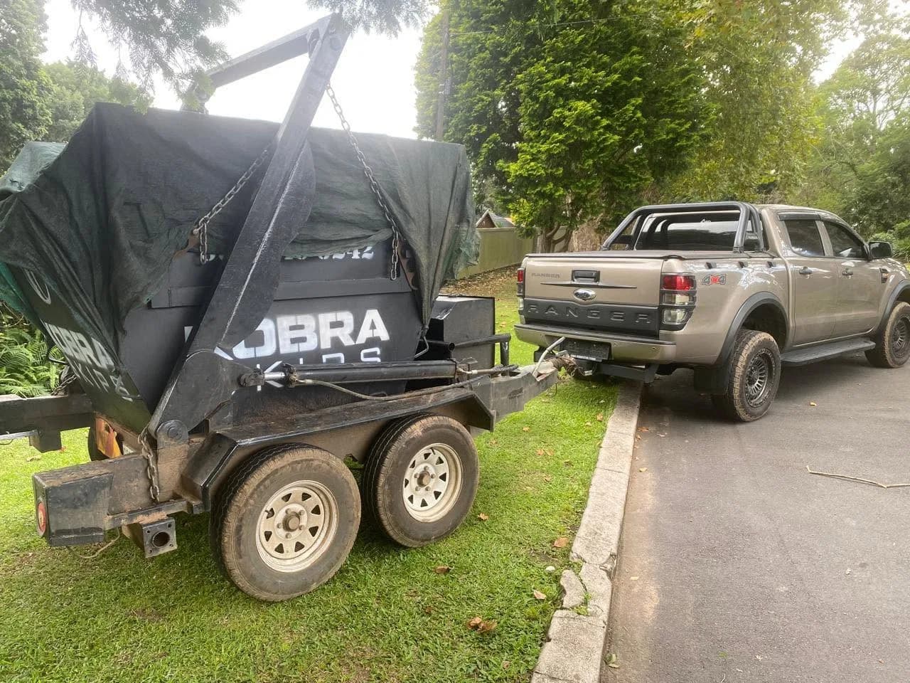 Covered Kobra Skip being towed by the Ford Ranger down a tree-lined suburban driveway.