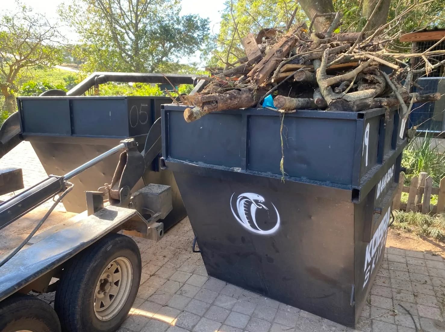 Kobra Skip filled with tree branches and garden debris being lifted onto the trailer for collection.