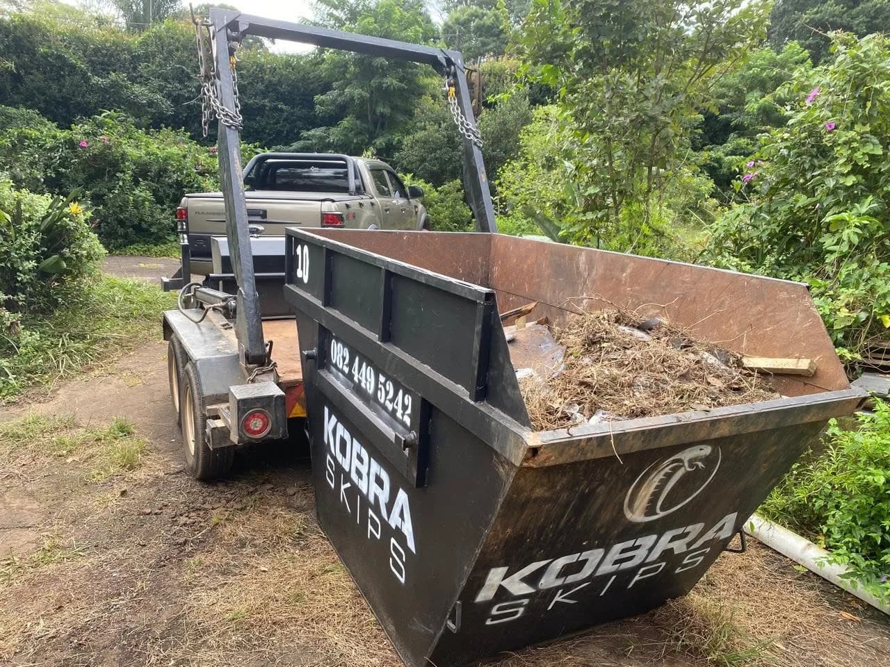 Kobra Skips truck collecting a skip loaded with garden soil and green waste from a property.