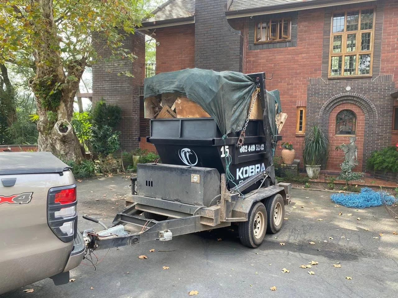 Covered Kobra Skip on a trailer outside a large brick home in Westville, being collected after a clearout.